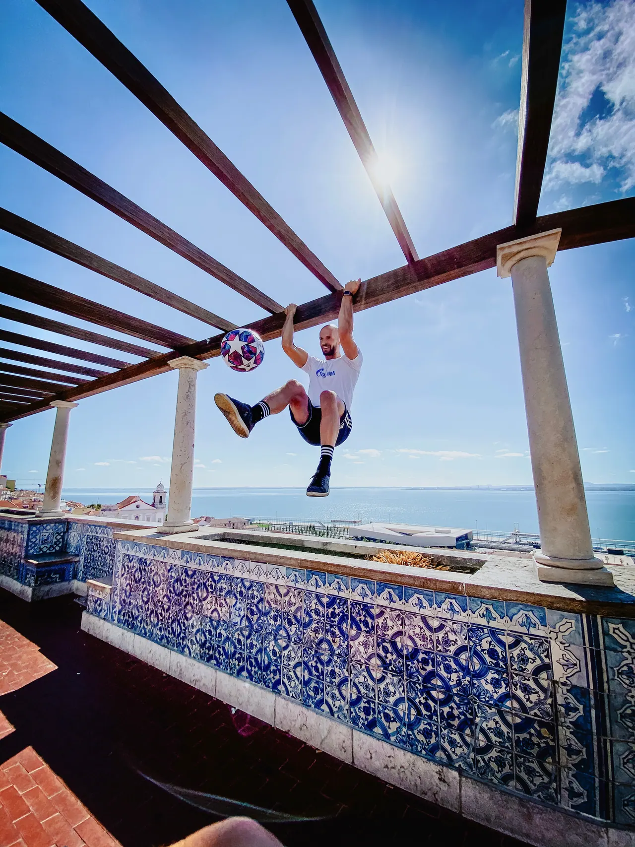 Daniel hanging from a pergola with a ball on his foot